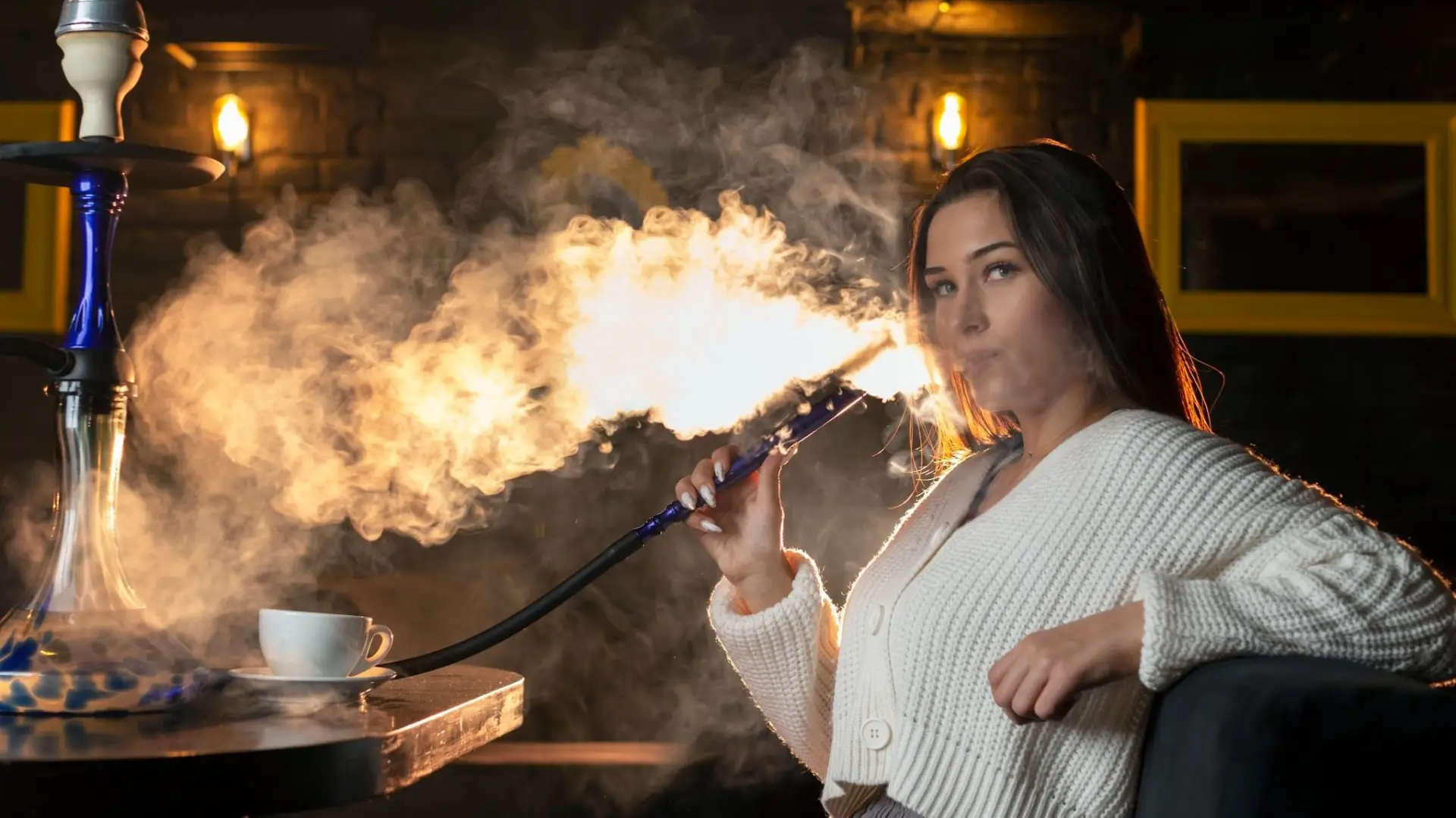 A young woman enjoying shisha at a clean, modern hookah lounge in Toronto, showing a relaxing hookah experience while listening to music.